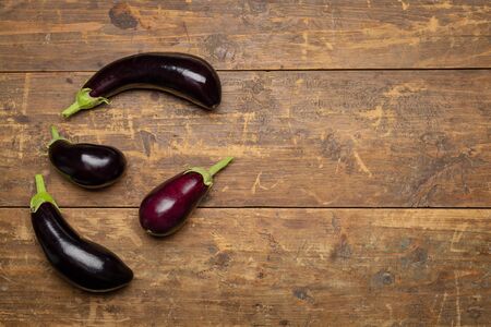Freshly picked raw eggplants on warm old rustic wooden background. Top view with space for textの写真素材