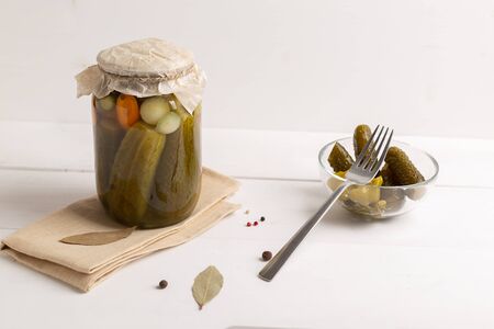 Canned fermented pickled cucumbers on white wooden background. Homemade cucumbers in a glass jar and glass bowlの写真素材