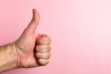 Male hand with thumb upwards on a pink background with copy space.の写真素材