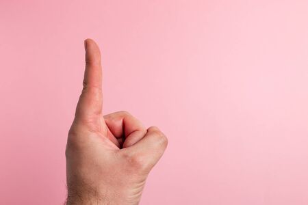 A male hand with the index finger pointing up with copy space on pink backgroundの写真素材