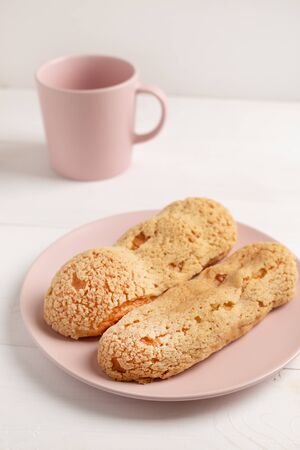 Homemade Eclair with craquelure on the plate and empty pink mug on light background.の写真素材