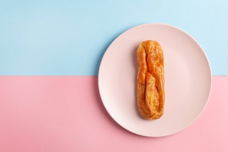 Homemade Eclair with craquelure on the plate on Blue and pink pastel background.