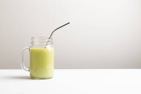 Matcha green tea latte in glass jar with metal tube on white backgroundの写真素材
