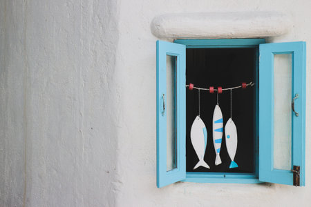 Charming pastel blue window with decorative fish mobile on white plaster wall in Mediterranean...