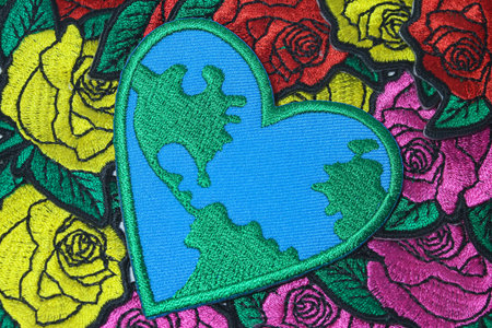 Close-up of handcrafted embroidery featuring a heart with world map pattern on a colorful rose...
