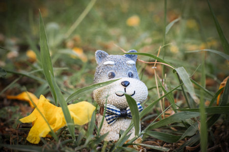 Close-up macro view of a tiny clay dog figurine with a bowtie, happily surrounded by fallen flowers and green grass. Soft natural background, portraying harmony with nature.の写真素材