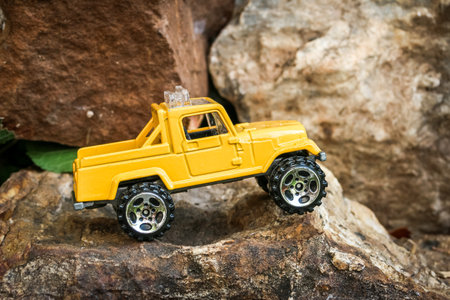 Yellow miniature 4x4 truck parked on uneven rocky ground right at the edge of a cliff in a small-scale adventurous scene. Fun, creative off-road concept for imaginative explorationの写真素材