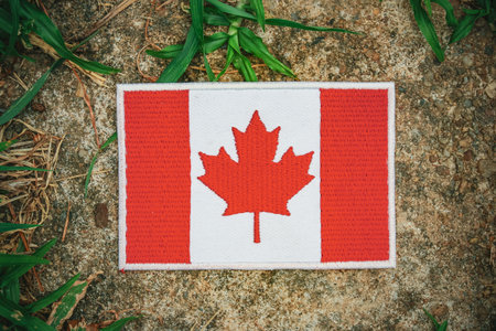 Embroidered Canada flag on rustic stone with grass and leaves, symbolizing eco friendly harmony and natural calmness , vintage toned.の写真素材