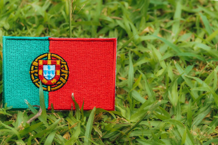Embroidered Portugal flag (PT) on grass under warm natural light. Symbol of sustainability, Earth Day and climate change awareness.の写真素材