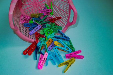 Playful design Bright plastic clothespins spilling from pink basket on teal background. Vibrant household items in playful, pop art flat lay composition.の写真素材