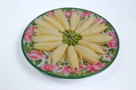 White fragrant champak flowers arranged in circle on vintage floral ceramic plate. Spa-inspired still life with natural Thai elegance.の写真素材