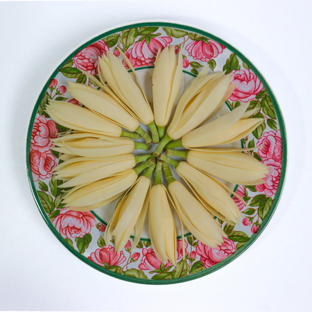 Circle of white champak flowers on antique ceramic plate with floral design, top view. Classic Thai still life, elegant and calming style.の写真素材