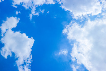 Blue sky background Natural tropical sky with white clouds and sunlight filtering through. Low angle blue-sky view expressing calm, summer light, and peaceful outdoor mood.の写真素材