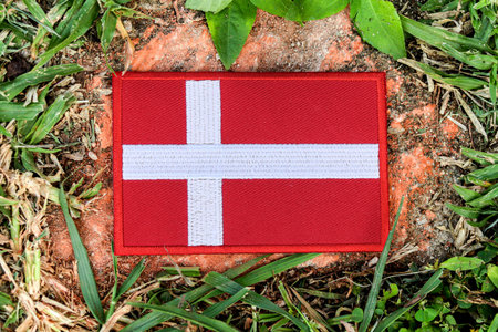 Horizontal photo of Danish flag made with fabric and thread on stone, wrapped in greenery.の写真素材