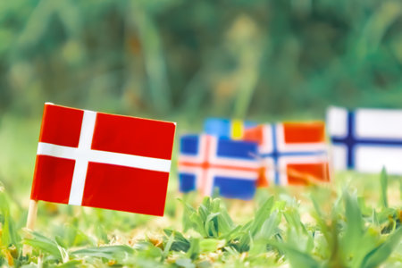 Flag of Denmark planted in fresh grass, positioned left. Soft blur of Nordic flags on the right. Eco-friendly, nature, and green travel themed image.の写真素材