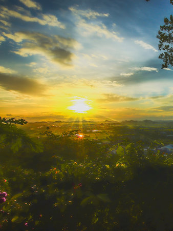 Peaceful mountain sunset view in Thailand with golden sunlight, leafy foreground, and dramatic twilight clouds. Nature therapy and travel inspiration.の写真素材