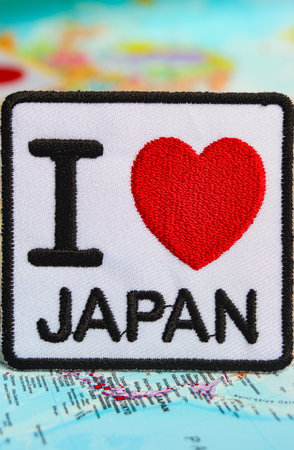 Eco-textile with "I LOVE JAPAN" and a heart in red thread, placed on a map pinpointing Japan. Represents national pride, sustainable travel, and green tourism.の写真素材
