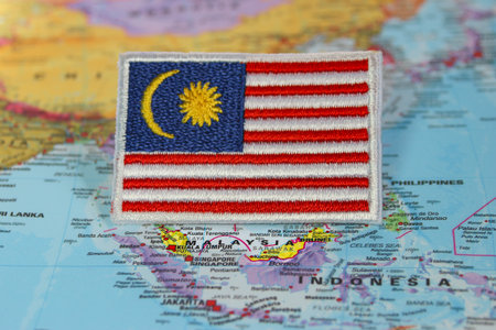 Hand-embroidered Malaysian flag in red, white, blue, and yellow threads on fabric, placed on map marking Southeast Asia. Travel, eco-tourism, culture concept.の写真素材