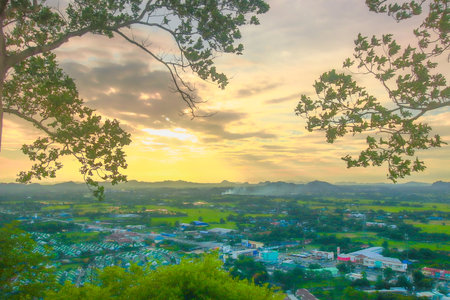 Golden sunset over countryside with homes, farmlands, and distant hills, framed by tree branches. Serene, natural, and perfect for travel themes.の写真素材