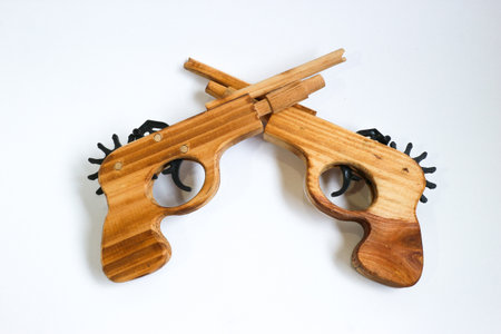 Wooden pistols with contrasting grain textures crossed in an X shape on a white studio background. Artistic concept of conflict, duality, and traditional craft.の写真素材