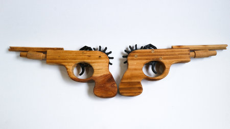 Wooden guns with unique patterns face left and right, joined at the handles. Displayed on a white background, representing artistic contrast and symmetry.の写真素材