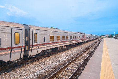 Passenger train on a graceful curve toward a small town, with gravel-lined rails and a bright blue...