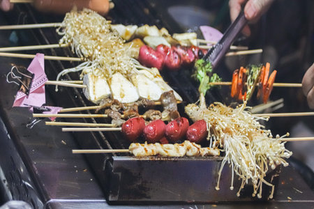 Bustling Thai night market with spicy mala skewers. Meat, mushrooms, sausage, and vegetables grilled over hot coals create a flavorful street food experience.の写真素材