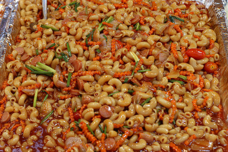 Thai macaroni pasta with sausage and tomato sauce in foil tray, garnished with scallion, carrot, and cherry tomato, classic street food dish.の写真素材