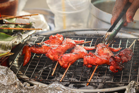 Grilled chicken wings with red glaze on bamboo skewers over smoky charcoal, Thai street food night market culinary vibe with authentic local taste.の写真素材