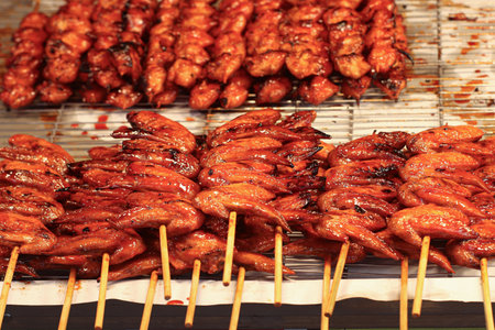 Thai-style grilled chicken wings on skewers with shiny red sweet sauce, caramelized texture, capturing authentic Asian street food and gastronomy tourism.の写真素材