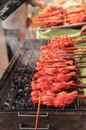 Grilled chicken ribs skewers on hot charcoal fire, smoky flavor and red marinade glaze, authentic Asian street food in a lively night market atmosphere.の写真素材