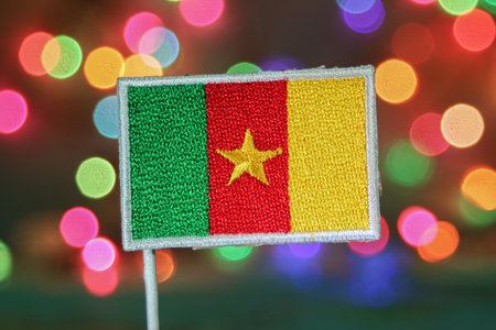 Embroidered Cameroon flag with rainbow bokeh fireworks background, symbolizing national day, holiday, and colorful New Year celebration theme.の写真素材