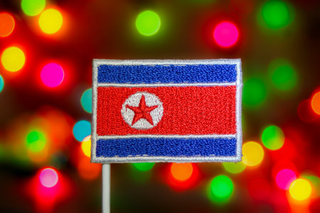 Eye-catching North Korea flag with a sewn finish, on a background of luminous, multi-colored bokeh lights. Ideal for national holidays, Asian politics, and festive visuals.の写真素材