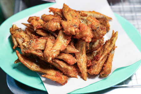 Deep-fried Chicken Wing Tips on a blue plate. Golden and crispy, a popular, savory, and easily available Thai street food snack.の写真素材