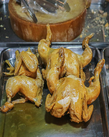 Traditional Whole Chicken (Kai Tom Nam Pla) braised in fish sauce. Golden, tender, and savory Thai street food on a serving tray with kitchen tools.の写真素材