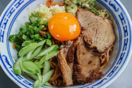 Close-up of savory Thai Red Pork Noodle with raw egg yolk and char siu. A rich, visually appealing, and authentic Thai-Sichuan street food.の写真素材