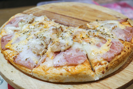 Close-up of a ham, sausage, and cheese Pizza (6 slices left) on a wooden tray. A popular and satisfying Thai street food item with melted cheese and golden crust.の写真素材