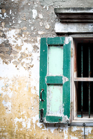 Vertical shot of an old green wooden window on a textured wall. The vintage Art Deco design and peeling paint create a charming, rustic architectural background.の写真素材