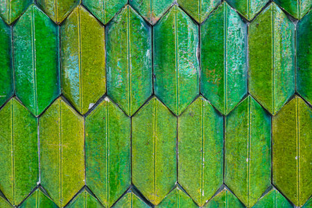 Glossy green-yellow ceramic tiles in a vertical herringbone pattern. Close-up texture, Thai temple...