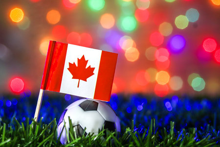 Flag of Canada beside soccer ball on field with blue spotlight and rainbow bokeh. Ideal for sport ads, global events, and Canada tournament promotion.の写真素材