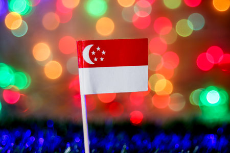 Singapore flag with crescent & stars illuminated by rainbow bokeh lights, symbolizing festive spirit, national pride, tourism energy, cultural celebration, & modern city identity.の写真素材
