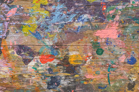 Vivid paint splatters on weathered wood create an energetic artistic texture, perfect for design projects, DIY themes, and creative workshop backgrounds.の写真素材