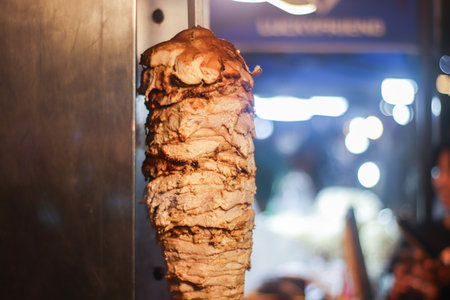 Vertical rotisserie Shawarma Kebab meat. Authentic Middle Eastern street food and global comfort food. Dynamic night market setting with vibrant bokeh background.の写真素材