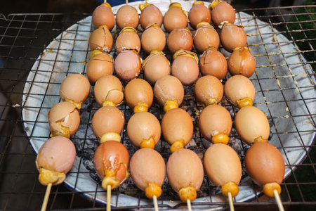 Thai grilled seasoned eggs on skewers over charcoal. Authentic Kai Song Kreung street food, nutritious protein snack, and traditional Asian culinary culture.の写真素材