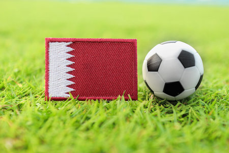 Qatar national flag beside soccer ball on green football field representing Middle East football...