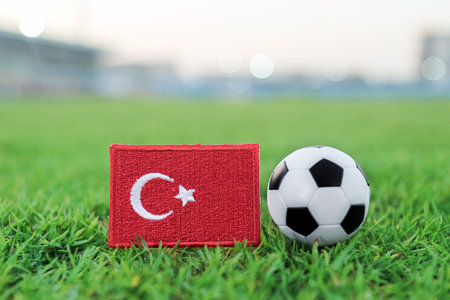 Turkey national flag beside soccer ball on green football stadium grass with blurred field...