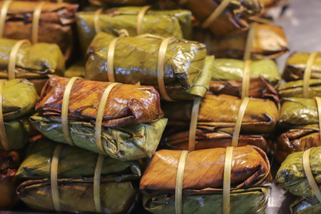 Sticky rice with banana filling wrapped in banana leaves stacked in rows showing traditional Thai...