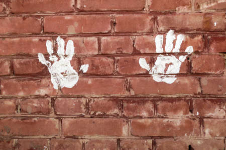 White prints of the palms of the hands on the brick wall
