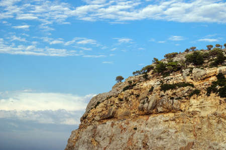 Steep rock with trees against a blue sky, Greece.の写真素材