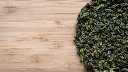 Top view dry green tea leaves on a wooden board.